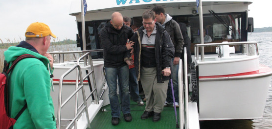 Mann mit Gehhilfen verlässt Veranstaltung auf dem Schiff und bekommt Unterstützung durch 2 weitere Männer.