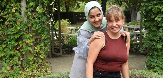 Zwei junge Frauen posieren zusammen für ein Foto, eine trägt ein Kopftuch.