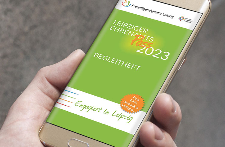Ein Smartphone in einer Hand mit dem Cover des Begleithefts zum Leipziger EhrenamtsPass 2023