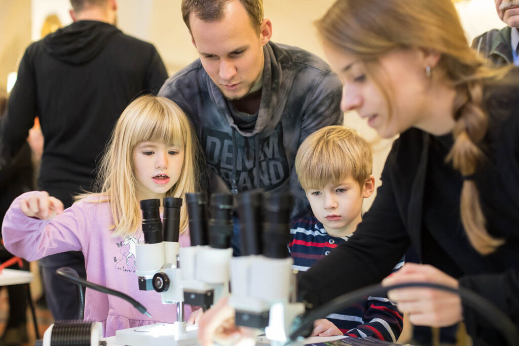 Foto einer Mitmach-Aktion bei der Engagementmesse 2019: Zwei Erwachsene und zwei Kinder mit Mikroskopen
