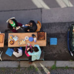 Menschen sitzen an Bierbänken auf einer freien Parkfläche und beschäftigen sich mit Gesellschaftsspielen.
