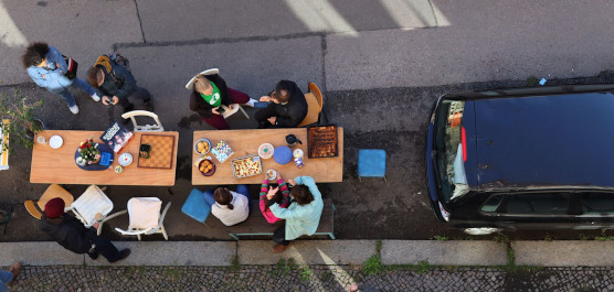 Menschen sitzen an Bierbänken auf einer freien Parkfläche und beschäftigen sich mit Gesellschaftsspielen.