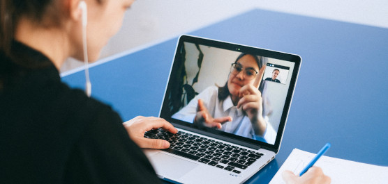 Eine junge Person sitzt vor dem Laptop und unterhält sich in einer Videokonferenz mit einer anderen jungen Person.