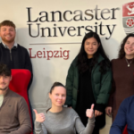 Eine Gruppe Studierender vor dem Logo der Lancester University