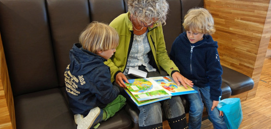 Eine ältere Person liest zwei Kindern auf einem Sofa aus einem Buch vor.