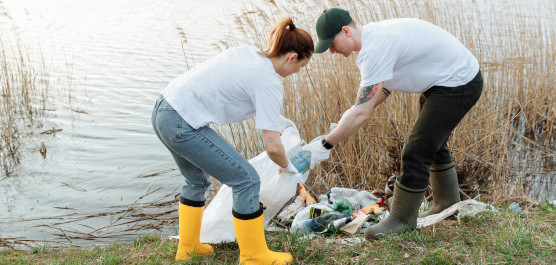 Zwei Ehrenamtliche sammeln Müll an einem See auf.